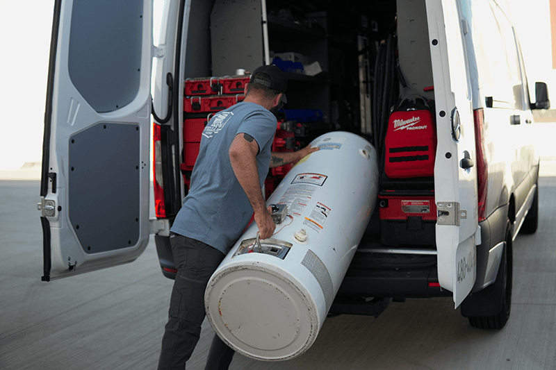 plumber loading tanked water heater into truck